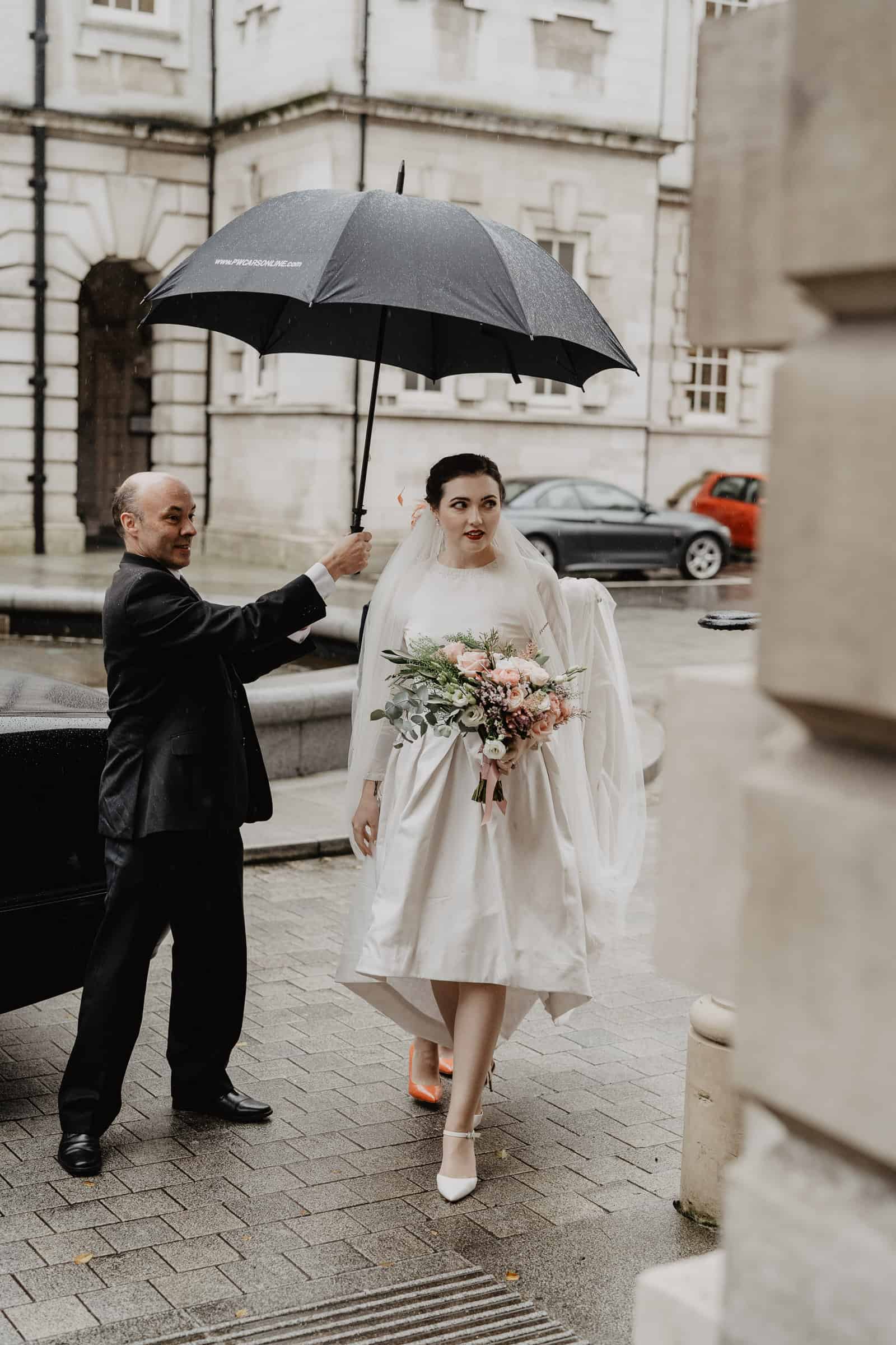 Bride walking into city hall with umbrella covering her